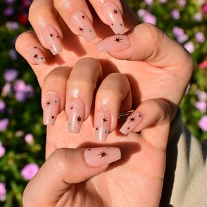 This nail set features a soft nude pink base adorned with delicate golden starbursts and colorful confetti details. Perfect for a playful yet elegant look that adds a touch of sparkle to any occasion.