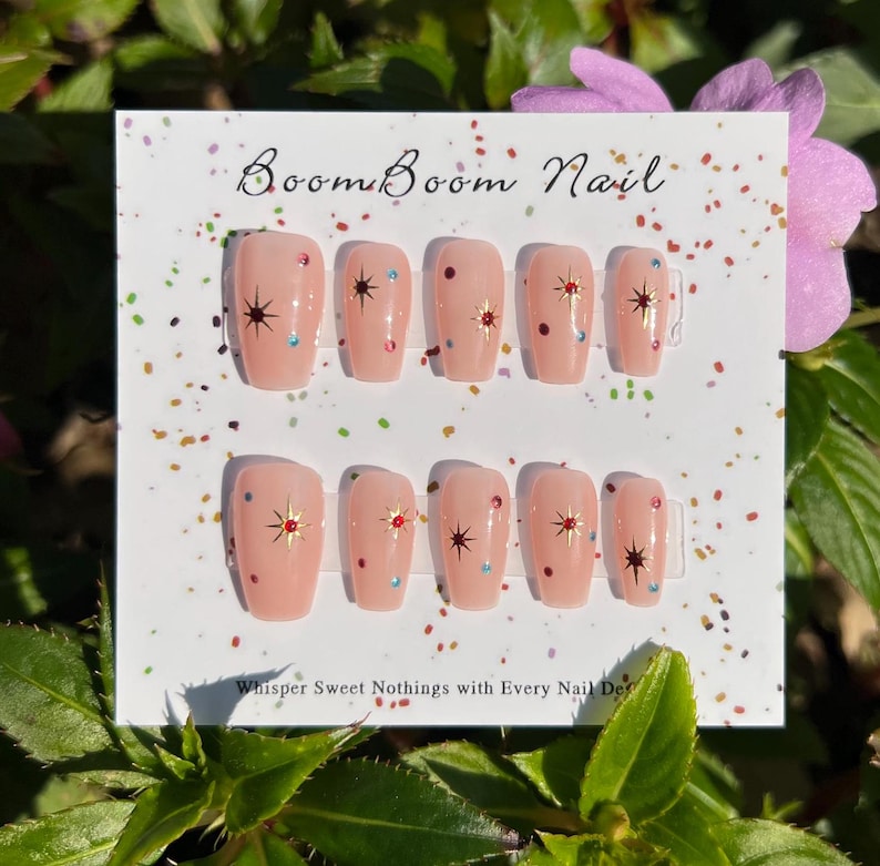 This nail set features a soft nude pink base adorned with delicate golden starbursts and colorful confetti details. Perfect for a playful yet elegant look that adds a touch of sparkle to any occasion.
