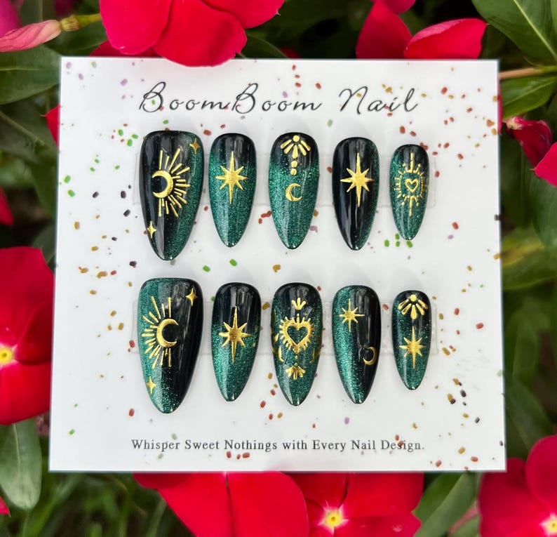 K&ouml;nnte beinhalten: Ein Set von Press-On-N&auml;geln mit einem schwarzen und smaragdgr&uuml;nen Glitzerdesign. Jeder Nagel zeigt goldene Himmelsmotive, darunter Monde, Sterne und Herzen. Auf der Karte steht "Boom Boom Nail" und "Whisper Sweet Nothings with Every Nail Design."