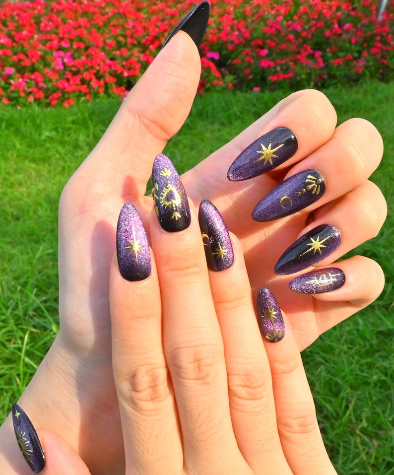 This nail design features a deep purple to black gradient base, adorned with gold celestial elements like the moon, sun, and stars, creating a luxurious and mystical vibe.