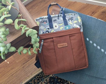 Understated floral print backpack with brown canvas and navy blue straps, zipper pockets on front and inside, double zip opening rucksack