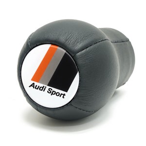Puede incluir: Pomo de cambio de marchas de cuero negro con un logotipo Audi Sport blanco, naranja y gris.