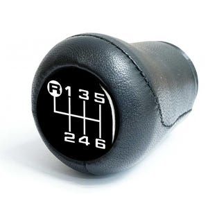 Op de afbeelding: Zwarte leren versnellingspookknop met een zwart-wit versnellingschema en de letters R, 1, 3, 5, 2, 4 en 6.