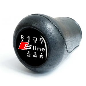 May include: Black leather gear shift knob with white gear numbers and the S line logo in red and white. The gear pattern includes reverse, 1, 2, 3, 4, 5, and 6. The knob is designed for a vehicle.