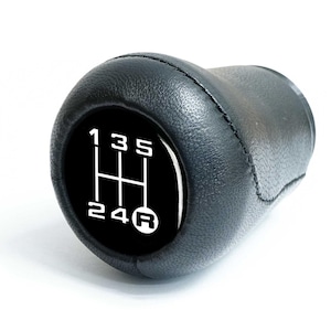 Könnte beinhalten: Schwarzer Lederschaltknauf mit weißem Gangmuster auf schwarzem Hintergrund. Das Gangmuster zeigt die Zahlen 1, 3, 5, 2, 4 und R für den Rückwärtsgang.