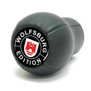 May include: Black leather gear shift knob with a black and white circular emblem that says "Wolfsburg Edition" with a red and white castle graphic inside.