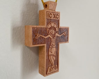 May include: A wooden cross with a carved image of Jesus Christ. The cross is brown and has a gold cord attached to the top. The inscription "IC XC" is carved on the cross.