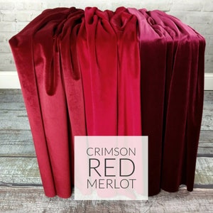 May include: A display of three velvet fabrics in shades of red: crimson, red, and merlot. The fabrics are draped over a surface, showcasing their texture and color variations. The image includes a white square with the text "CRIMSON RED MERLOT".