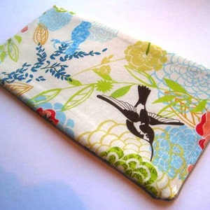 May include: A white zippered pouch with a floral print featuring a hummingbird, green leaves, and blue, yellow, and red flowers.