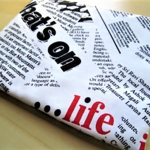 May include: White fabric with black and red text. The text reads "That's on life". The fabric has a newspaper print design.