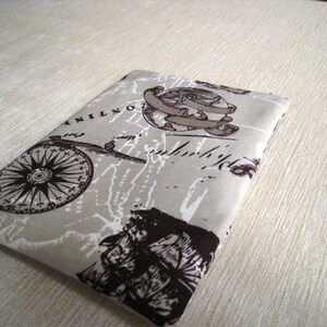 Puede incluir: Una funda de tela beige con un diseño vintage de mapa y brújula. La funda presenta una rosa de los vientos, un globo terráqueo con una pancarta y detalles de mapa en marrón y blanco. La tela tiene un aspecto ligeramente texturizado.