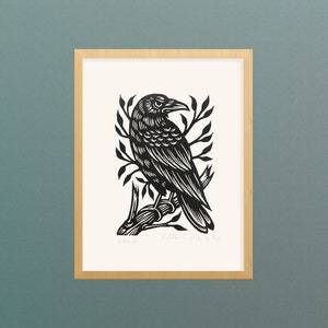 May include: Black and white woodcut print of a crow perched on a branch. The print is framed in a light wood frame and has the year "2012" and the artist's name "Jack  Smith" in the bottom left and right corners.