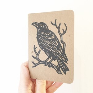May include: A brown paper notebook with a black ink illustration of a crow perched on a branch.