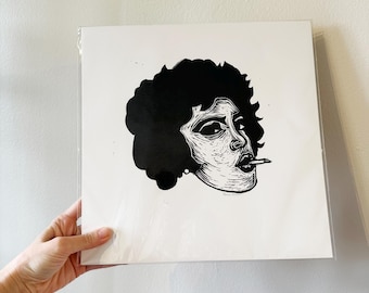 May include: Black and white art print featuring a stylized portrait of a person with curly hair, smoking a cigarette. The artwork is a linocut print, with bold lines and a high-contrast design. The print is held in a clear plastic sleeve.