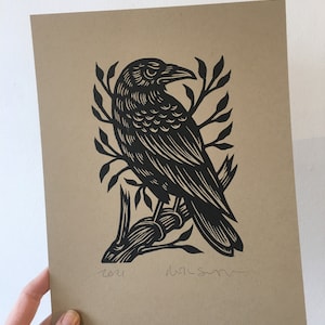May include: Black and white linocut print of a crow perched on a branch. The print is signed and dated "2021".