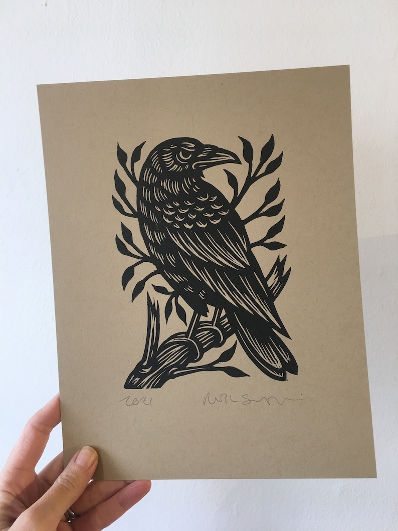 May include: Black and white linocut print of a crow perched on a branch. The print is signed and dated "2021".