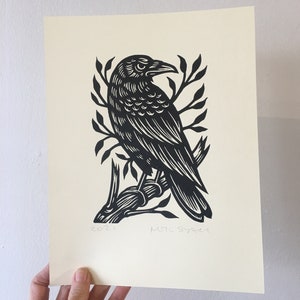 May include: Black and white linocut print of a crow perched on a branch. The print is signed "MTL SYNER" and dated "2021".