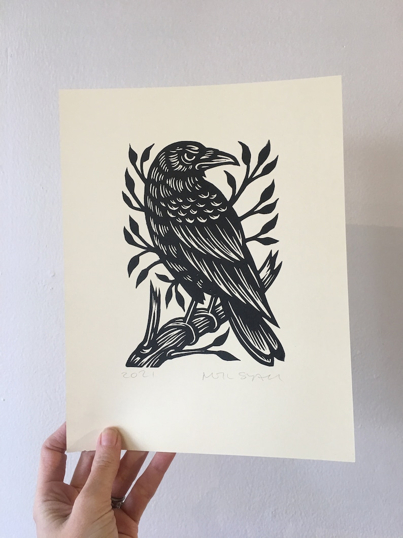 May include: Black and white linocut print of a crow perched on a branch. The print is signed "MTL SYNER" and dated "2021".