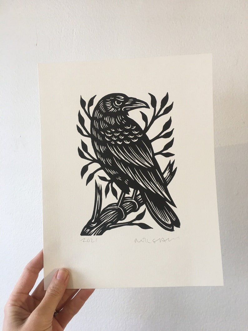 May include: Black and white linocut print of a crow perched on a branch. The print is signed and dated 2021.