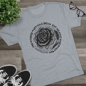 Puede incluir: Una camiseta gris jaspeada con una impresión negra de una rosa y el texto "Too Roses Too, Rose S. Schwamtorian - The Worker Must Have Bread But She Must Have Roses Too."