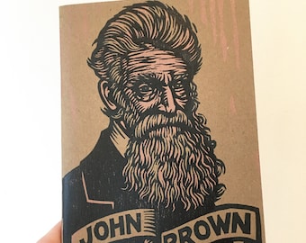 May include: A brown paper notebook with a black and white illustration of John Brown. The illustration is in a woodcut style and features a detailed portrait of John Brown with a long beard. The text "JOHN BROWN" is printed in black on a white banner.
