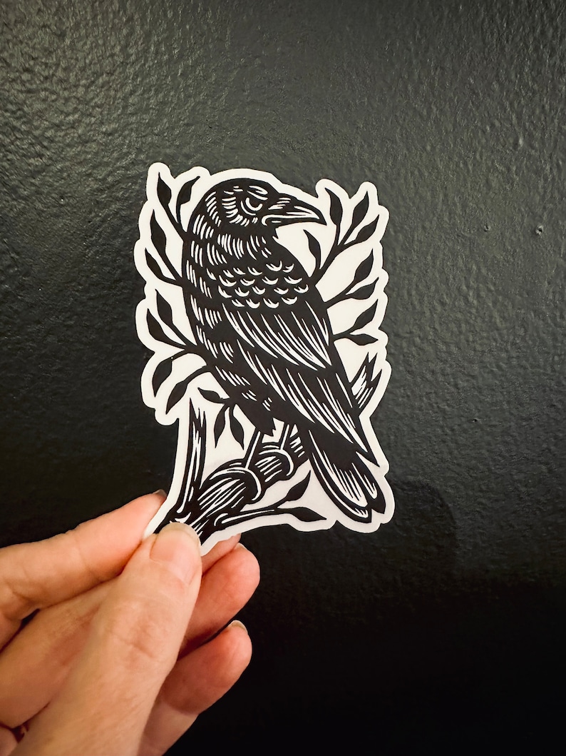 Peut inclure: Autocollant noir et blanc d'un corbeau perch&eacute; sur une branche. Le corbeau est d&eacute;taill&eacute; avec des plumes et a un bec pointu. La branche a des feuilles et est stylis&eacute;e.