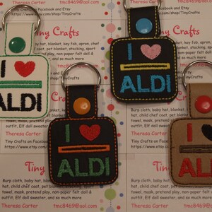 May include: Four keychains with the text "I love ALDI" in different colors and designs. The keychains are made of felt and have a heart shape in the middle.
