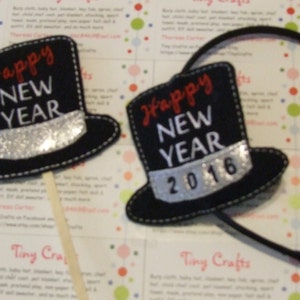 May include: Two black felt top hat photo booth props. One hat says "Happy New Year" and is on a stick. The other hat says "Happy New Year 2016" and is attached to a black headband.