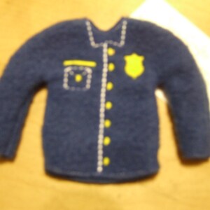 May include: A blue felt shirt with a white trim and yellow buttons. The shirt has a badge on the front with a yellow star.