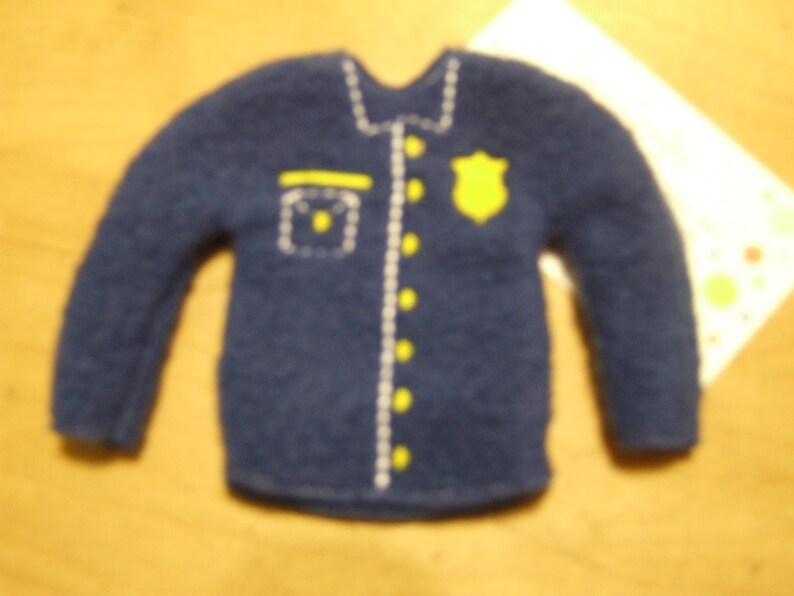 May include: A blue felt shirt with a white trim and yellow buttons. The shirt has a badge on the front with a yellow star.