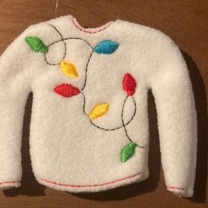 May include: White fleece elf sweater with a red, yellow, green, and blue string of lights embroidered on the front.