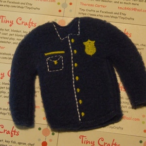 May include: A blue felt police officer's jacket with yellow stitching and a gold badge. The jacket is a felt applique for a doll or craft project. Tiny Crafts on Facebook and Etsy, tmc8469@aol.com