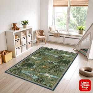 Könnte beinhalten: Ein rechteckiger grüner Teppich mit einer detaillierten Waldszene mit Bäumen, Tieren und einem Fluss. Der Teppich hat einen dunkelblauen Rand und liegt auf einem hellen Holzboden. Der Teppich befindet sich in einem Raum mit einem Fenster und einem weißen Aufbewahrungsmöbel.