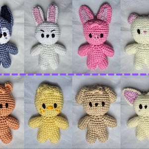 May include: A collection of eight handmade crochet animal figures. The figures include a blue wolf, white bunny, pink pig, cream bear, orange bear, yellow chick, tan dog, and cream bat. Each figure has black eyes and a unique expression.
