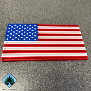 May include: A 3D-printed American flag in red, white, and blue. The flag features a blue canton with white stars and red and white stripes. The design is a stylized, rectangular representation of the U.S. flag.
