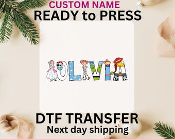 May include: A white background with the name "OLIVIA" spelled out in colorful letters. Each letter is decorated with characters from the Toy Story movie franchise. The text "CUSTOM NAME READY to PRESS" is at the top of the image. The text "DTF TRANSFER Next day shipping" is at the bottom of the image.