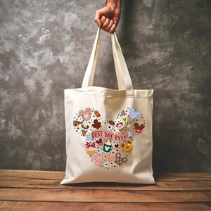 May include: A white canvas tote bag with a Mickey Mouse head design featuring various Disney-themed icons and the text "Best Day Ever!" in pink.
