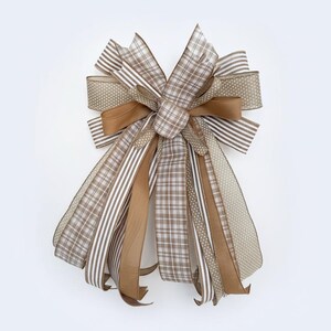 May include: A decorative bow featuring a mix of patterned ribbons in shades of brown, tan, and white. The bow includes ribbons with stripes, polka dots, and plaid patterns. The bow is tied in the center with a matching fabric.