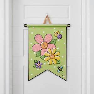 May include: A light green wall banner featuring a large pink flower, a yellow flower, and a small purple flower, each with a button center. The design includes white polka dots, a small flying bee, and a black border with a hanging wooden rod.