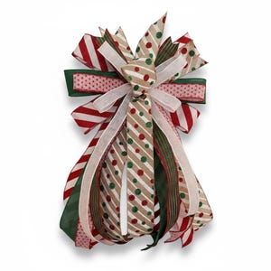 May include: A decorative Christmas bow with multiple ribbons in red, green, white, and tan. The bow features striped, polka dot, and solid patterns. The bow is designed with a layered effect, creating a festive and textured appearance, perfect for holiday decorations.