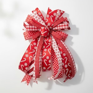 May include: A large, decorative Christmas bow featuring a variety of red and white patterned ribbons. The bow includes ribbons with polka dots, candy canes, and snowflake designs. The bow is a festive decoration.