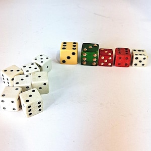 May include: A collection of dice in various colors, including white, yellow, green, and red. The dice are arranged in two groups, with the white dice in a pile and the colored dice in a row. Each die has black dots.