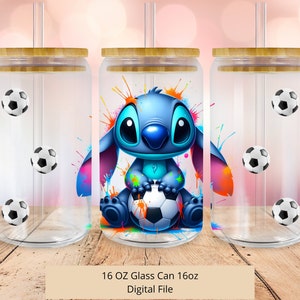 May include: A 16 ounce glass can with a blue and white cartoon character holding a soccer ball. The can has a bamboo lid and a straw. The background is a colorful splatter pattern.