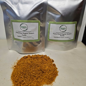 Peut inclure: Deux sachets argentés avec des étiquettes vertes contenant de la poudre de curcuma biologique séchée par congélation. L'étiquette indique "JENDEL ESSENTIALS Poudre de curcuma biologique séchée par congélation Ingrédients : Curcuma biologique 15 g". Un tas de poudre de curcuma est présenté au premier plan.