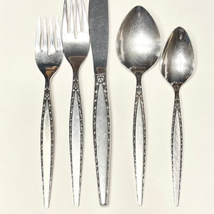 May include: A set of five silver-plated flatware pieces, including a knife, two forks, and two spoons. The flatware has a decorative pattern on the handles.