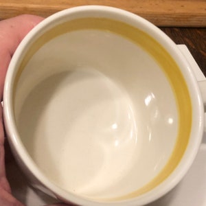 May include: White ceramic mug with a yellow band around the rim.