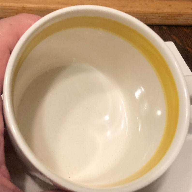 May include: White ceramic mug with a yellow band around the rim.