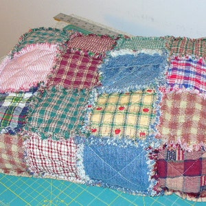 May include: A patchwork quilt made of various plaid and gingham fabrics in shades of red, blue, green, and yellow. The quilt is fringed and has a rustic, handmade look.