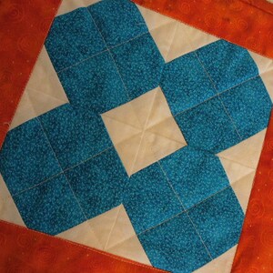 Puede incluir: Un cuadrado de tela acolchado con un patr&oacute;n geom&eacute;trico de cuadrados azul turquesa y crema. La tela est&aacute; bordeada con una tela naranja s&oacute;lida con un patr&oacute;n de espiral.