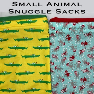 Puede incluir: Dos pequeños sacos para animales. Uno es amarillo con cocodrilos verdes, el otro es turquesa con monos grises con sombreros y bufandas rojas. Los bordes superiores son verdes y rojos, respectivamente. El texto "SMALL ANIMAL SNUGGLE SACKS" está en la parte superior.